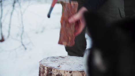 man splitting wood logs using axe in winter