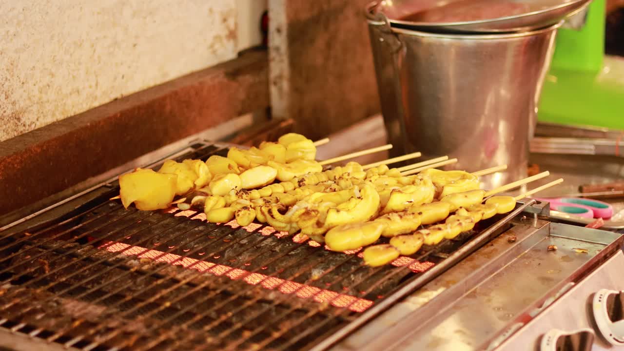 Grilled skewers on a street food grill in Bangkok. Warm lighting highlights the vibrant colors and textures of the food