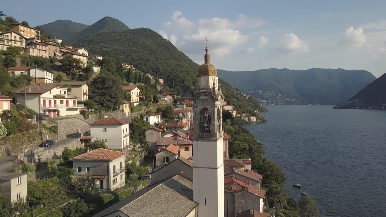 aerial de una torre del reloj de la iglesia en un pequeño pueblo en italia por un lago en el verano, nesso, lago como, italia