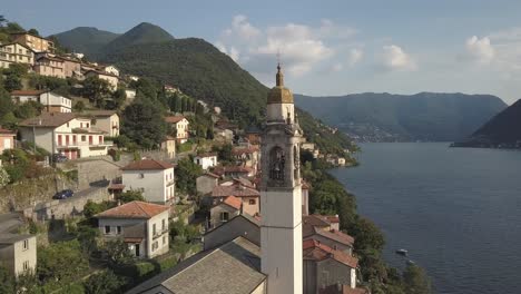 Aerial-of-a-Church-Clock-Tower-in-a-little-Village-in-Italy-by-a-lake-in-the-summer,-Nesso,-Como-lake,-Italia