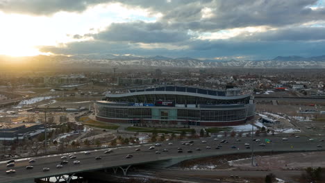 cinematic drone shot of iconic empower field at mile high formerly known as broncos stadium with a view of main street and snow capped mountain in background, colorado