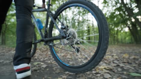 close up view of man's legs in black pants and white sneakers walking on the forest road with mountain bike