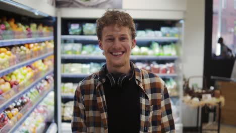 close up of the handsome young caucasian guy with headphones doing shopping in the supermarket and smiling cheerfully to the camera. portrait
