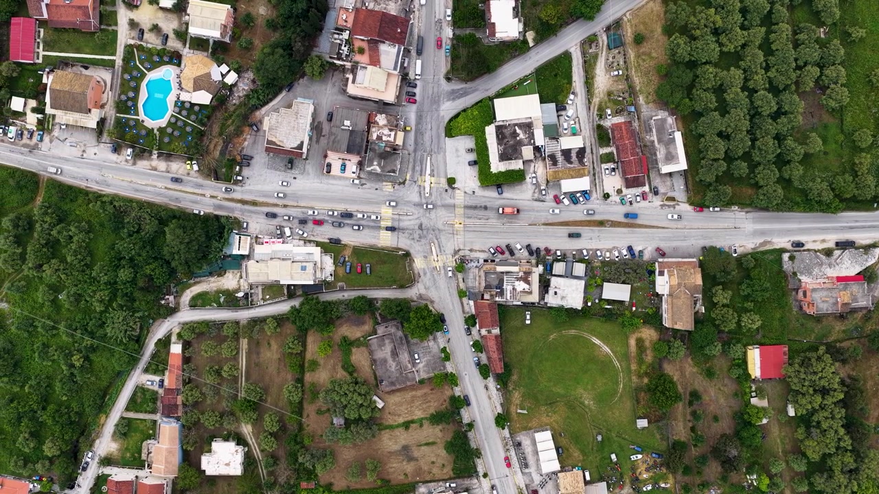 Ampia prospettiva aerea dall'alto di un trafficato incrocio stradale e del traffico veicolare nell'insediamento rurale di Roda, Corfù Nord, Grecia. Vista aerea con drone di case del villaggio e strade locali.