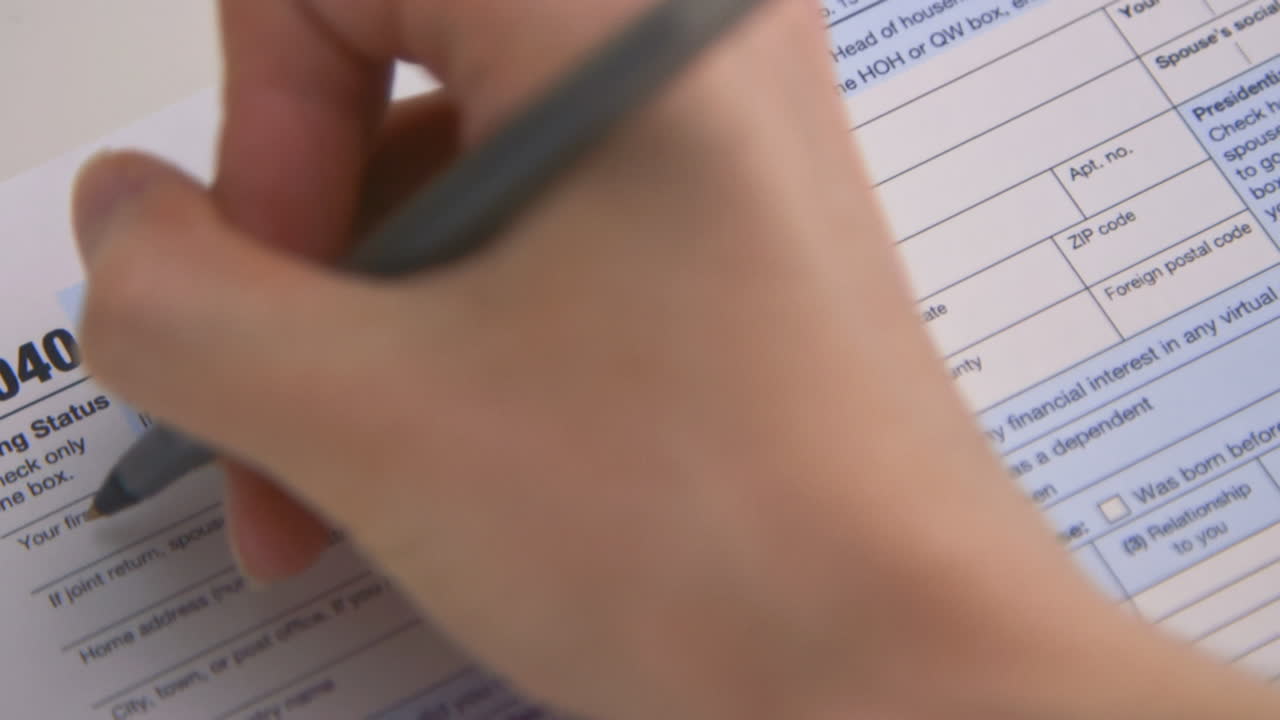 A caucasian woman's hand filling out her name on Tax Form 1040 for tax year 2020, for the IRS