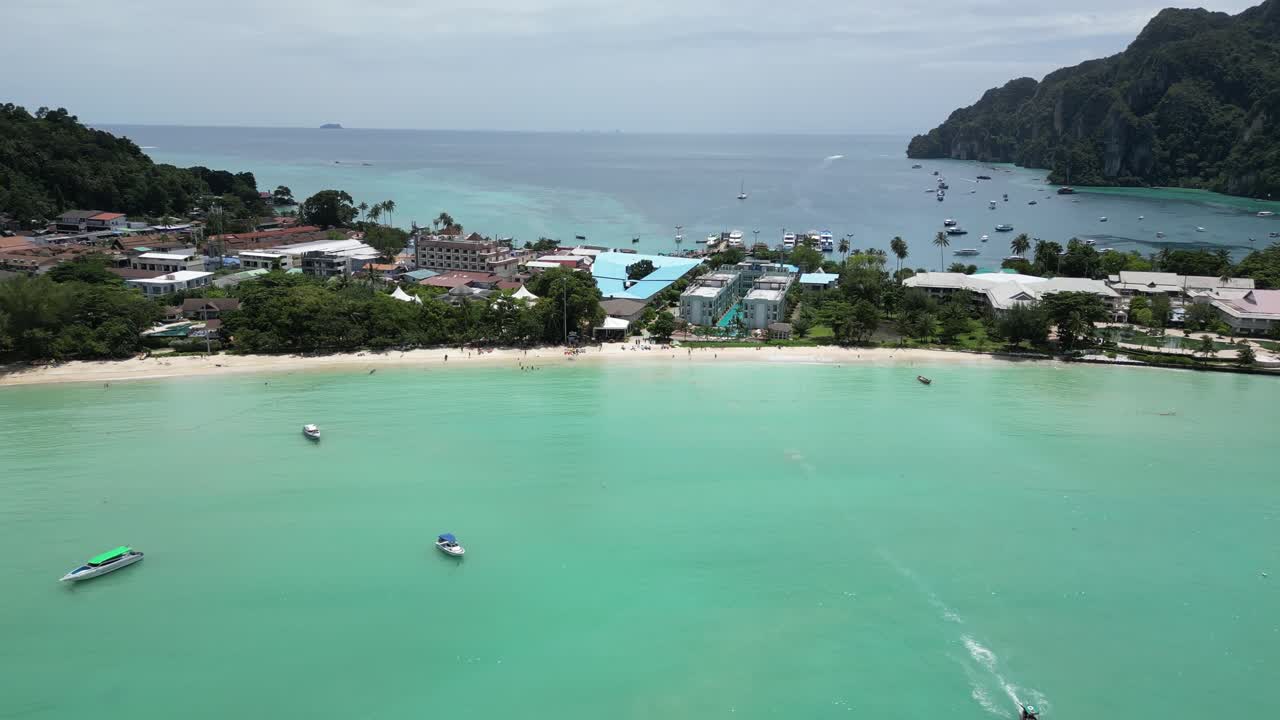 A forward-moving establishing aerial shot highlighting the beauty of Koh Phi Phi beach in Thailand, framed by turquoise waters.