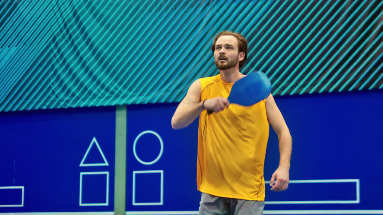 Man in yellow shirt playing pickleball on a blue, inside court