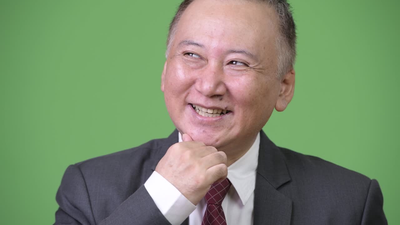 성숙하고 행복한 일본인 사업가가 생각하면서 웃고 있다.