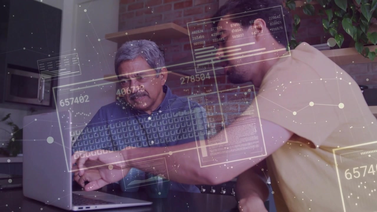 Adult son leaning pointing activating data overlays guiding senior using laptop in kitchen for tech