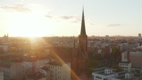 Red-Church-in-Berlin,-Germany-Neighbourhood,-Scenic-Wide-angle-Aerial-Shot-in-beautiful-golden-hour-Sunset-light,-Establishing-Shot