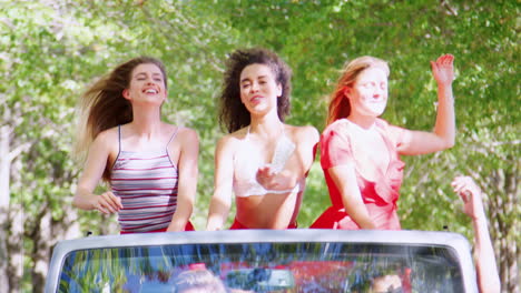 Girlfriends-standing-in-the-back-of-an-open-top-car-waving