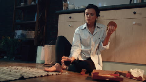 hungry woman eating burger with wine. girl enjoying fast food dinner at home.