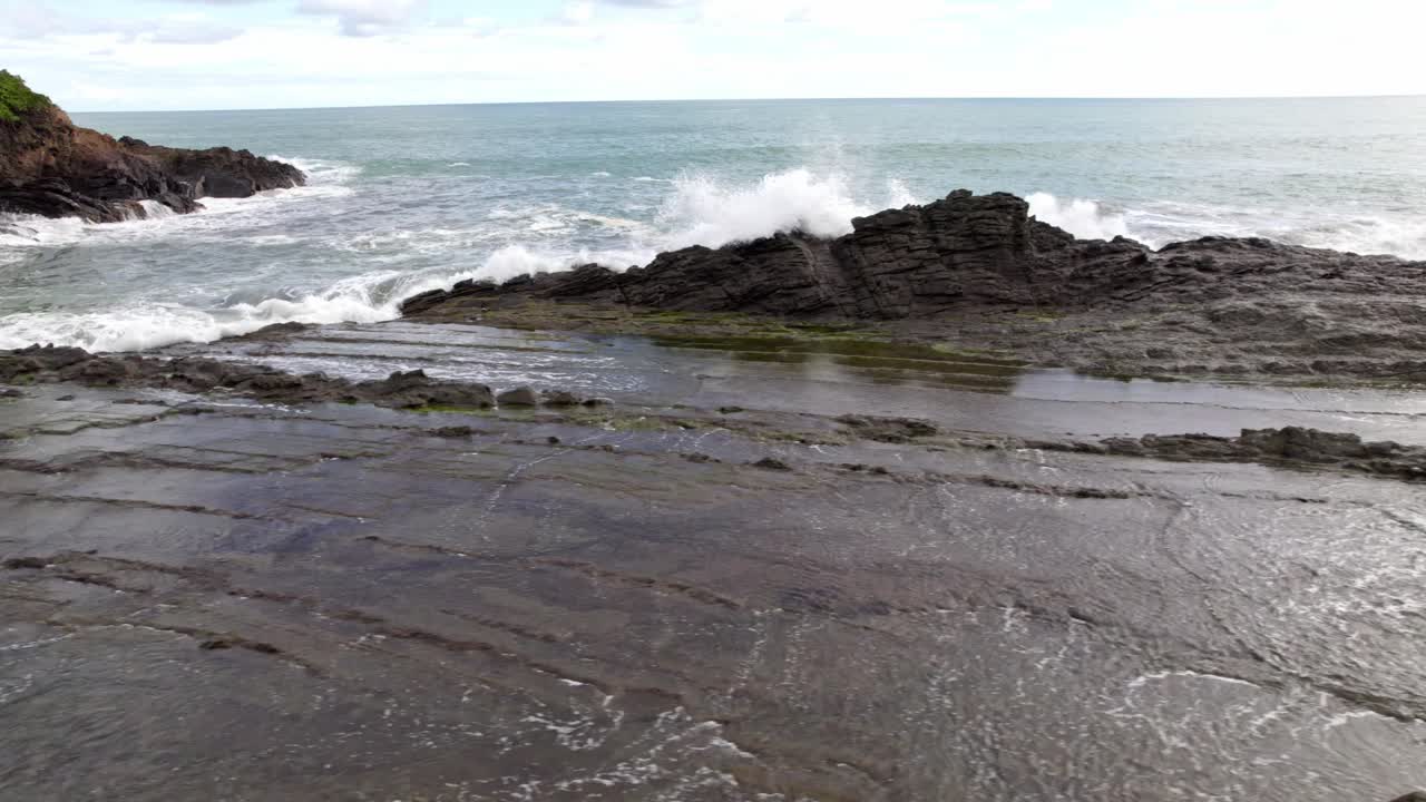Aerial truck left of foamy sea waves hitting the rocky coastline on a cloudy day in Dominicalito Beach, Costa Rica