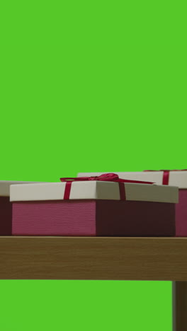 vertical video of presents in gift wrapped boxes on table shot against green screen