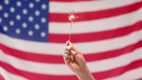 Close-up-of-hand-holding-sparkler-with-flag-of-usa-in-background