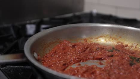 un chef agita una sartén llena de salsa de carne con un par de pinzas