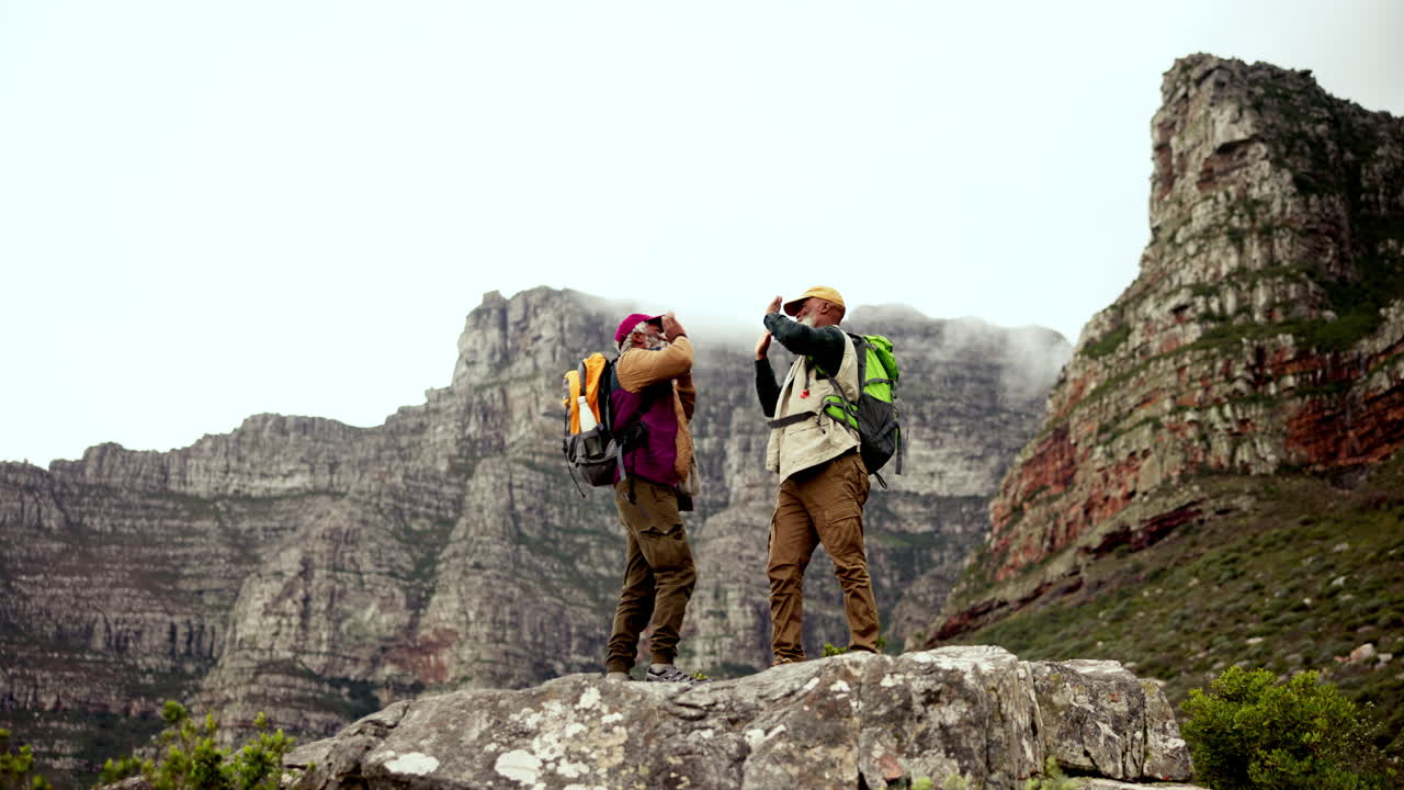 Two senior men celebrate on top of mountain