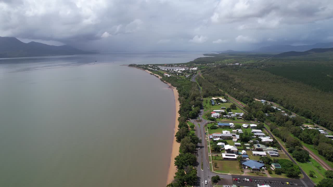 Aerial View of a Coastal Town with Beach, Ocean, and Mountains Under a Cloudy Sky