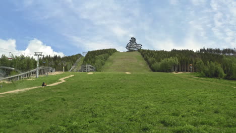 zooming aerial 4k shot of a four wheeler driving up a green slope heading towards the sky walk attraction in dolní morava, czechia with a cableway and forests around