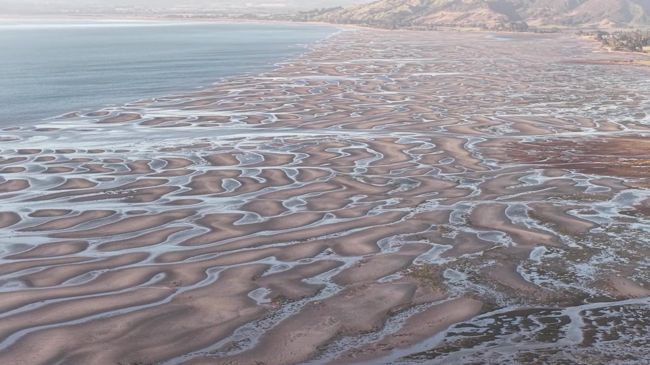 Aerial drone view of tidal sand patterns along South Island coastline in New Zealand, climate and abstract natural landscapes.