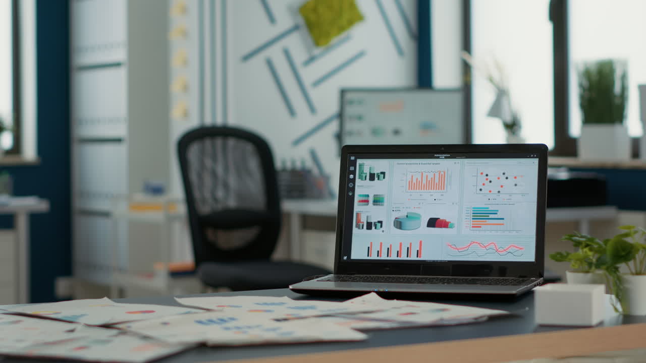 Ufficio di una startup vuoto con laptop che mostra software di gestione aziendale sullo schermo, con grafici e statistiche in movimento.