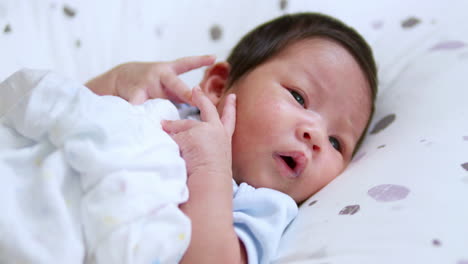 cute newborn baby touching her right ear and moving her fingers while she is listening to the voices of people surrounding her crib