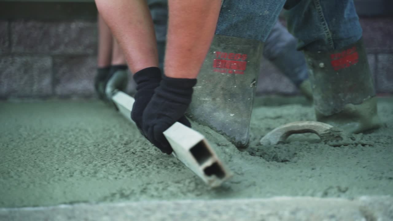 두 명의 익명의 건설 노동자들이 새로  ⁇ 은 콘크리트를 평준화  ⁇ , 느린 움직임으로 평준화하고 평준화합니다.