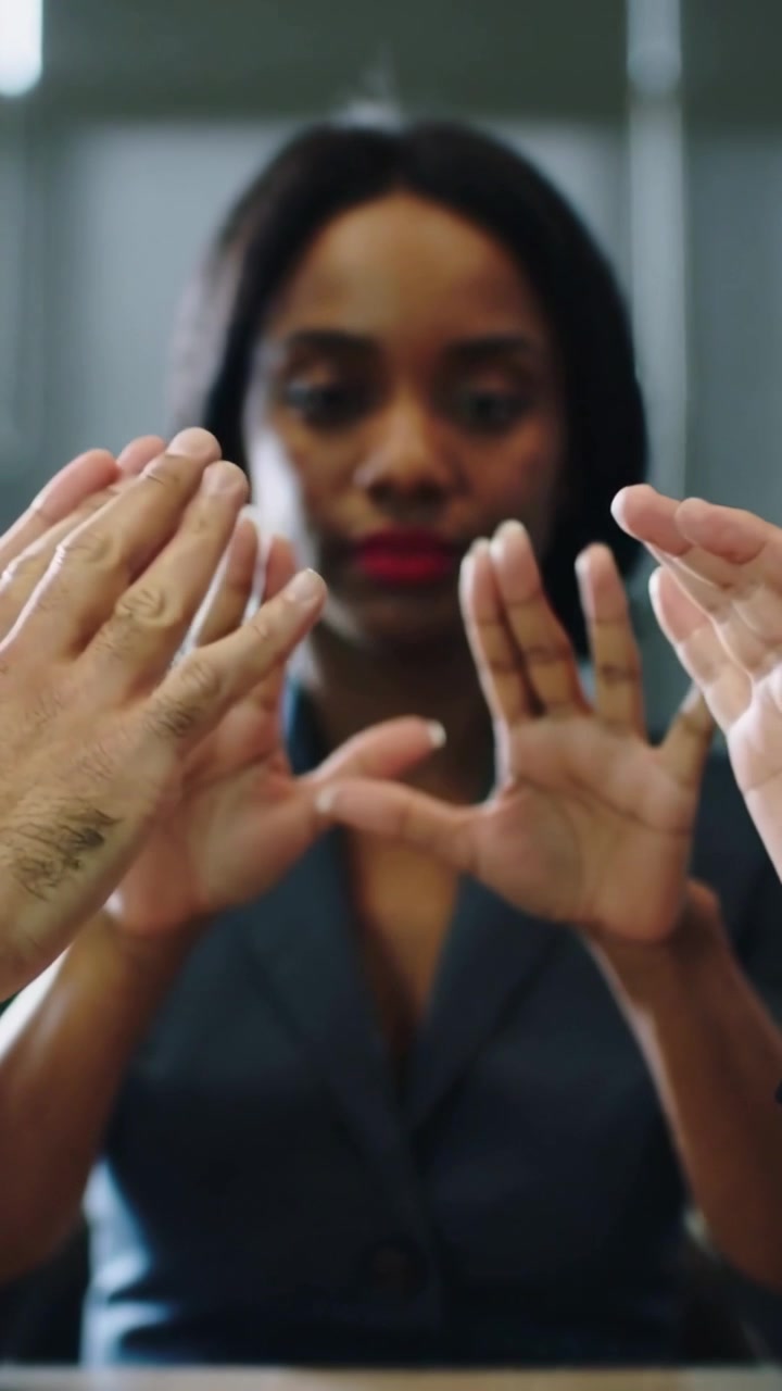 Vertical video: Entering hands forming triangle aperture at table, framing woman in dark blazer