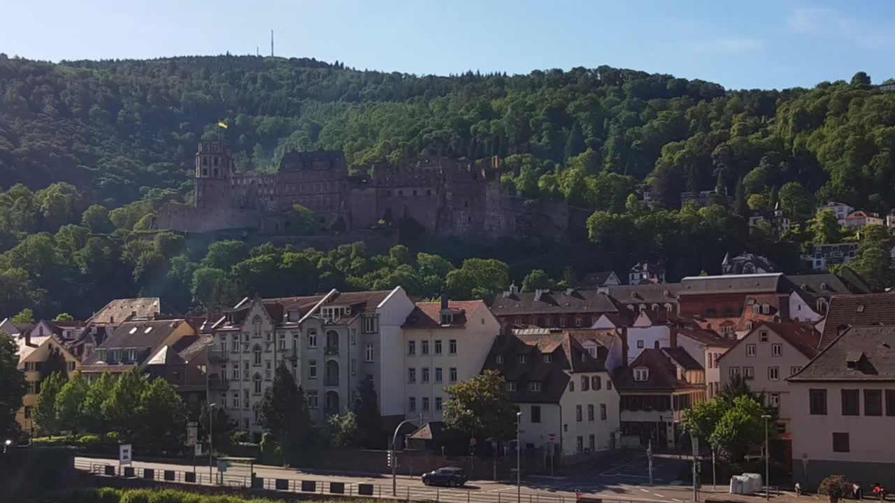 Vista statica del Castello di Heidelberg sulla montagna durante una giornata di sole, con edifici, strada e traffico in primo piano, Heidelberg, Germania