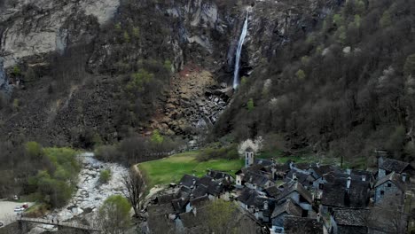 aerial flyover over foroglio in ticino, switzerland with a view of the village with old stone houses and waterfall in the background at dusk