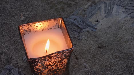 single lighted candle in metallic can, waving flame in wind