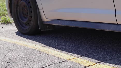 Macro-tight-shot-of-a-man's-boots-stepping-out-of-a-silver-car-on-a-sunny-day