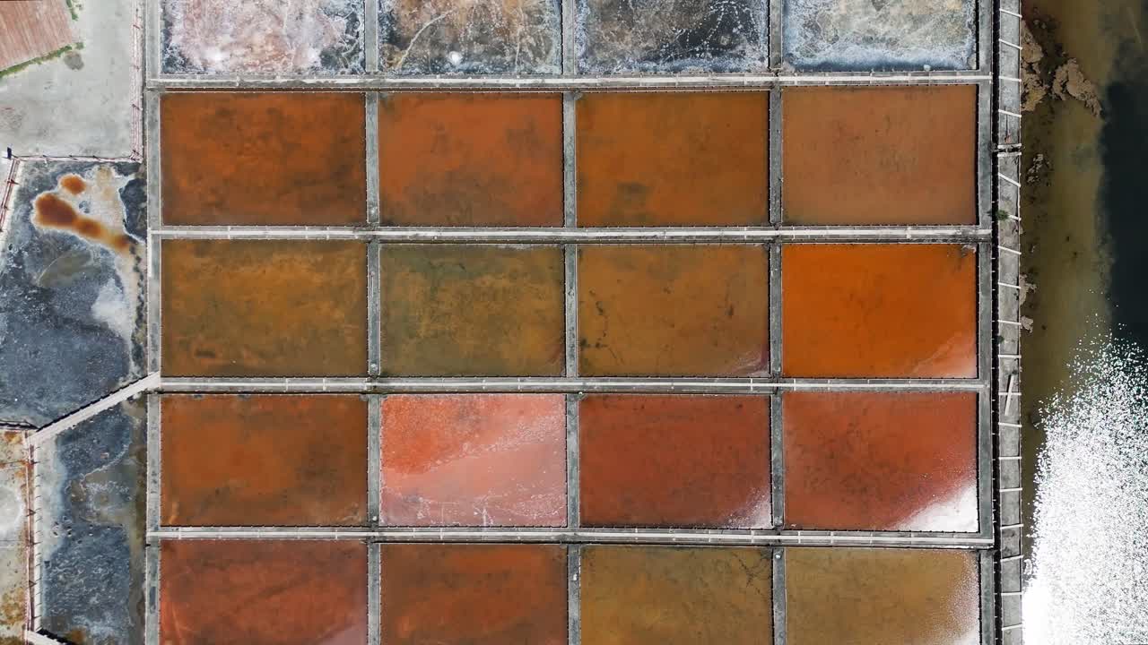 Drönarpanorering rakt ovanför symmetriska saltbassänger som visar livfulla naturliga färgvariationer