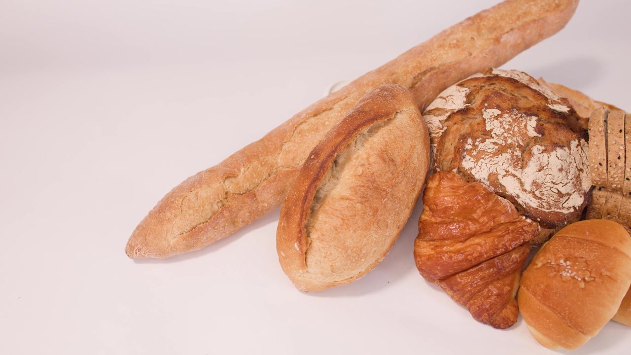 Inquadratura statica dall'alto di pane a lievitazione naturale, baguette, croissant e pane a fette sotto una luminosa illuminazione da studio.