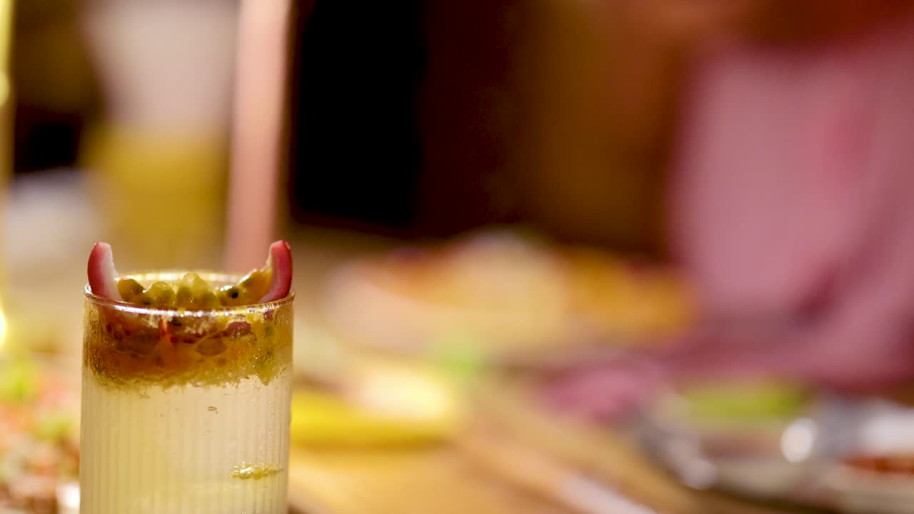Close-up of passion fruit soda glass, warm lighting, shallow focus, lively restaurant atmosphere, static shot