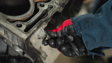 close-up of a hand in a red glove loosening a nut on a block engine, highlighting precision and detail in mechanical work within an automotive workshop