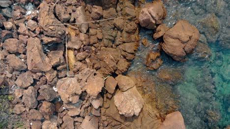 Tomas-De-Cámara-Marrón-Piedras-Mojadas-Con-Basura-Por-El-Borde-Del-Agua