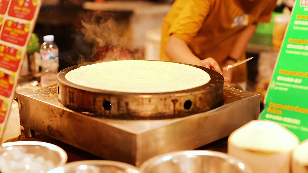 Persona che prepara crepes in una bancarella affollata del mercato di street food di Phuket