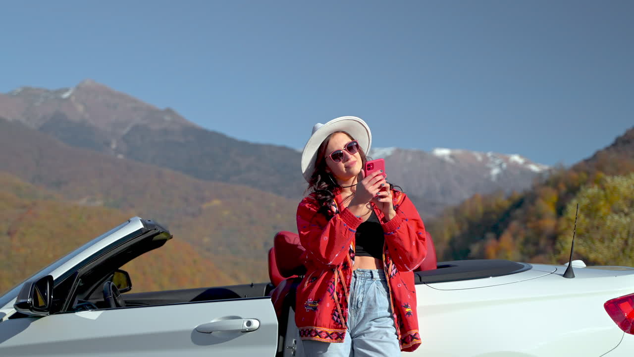 mujer usando el teléfono en un coche convertible con el fondo de las montañas