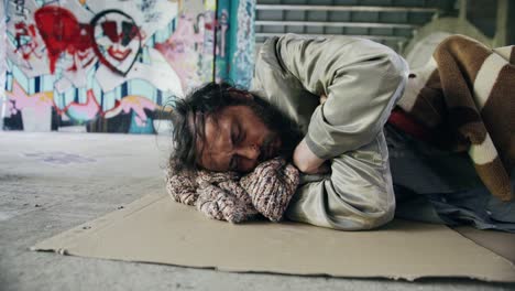 Homeless-man-sleeping-under-a-bridge-laying-on-a-piece-of-cardboard