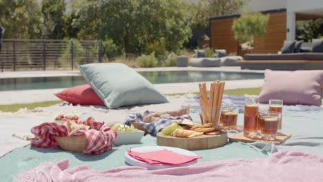 picnic blankets with pillows, food and drinks by pool in sunny garden, slow motion