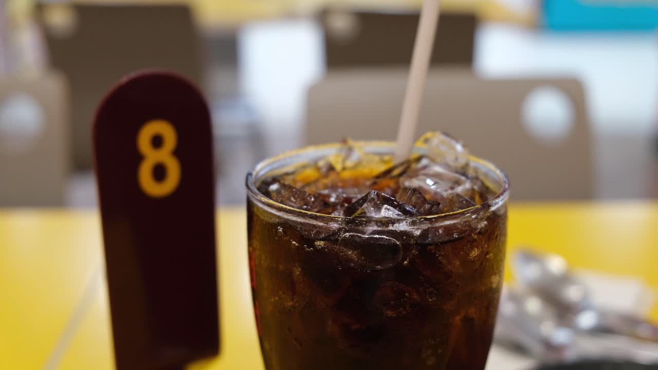 un vaso lleno de hielo y cola y una pajita sobresaliendo en una mesa luego un número de cola, comida y bebida