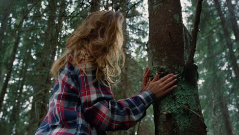 Woman-touching-tree-trunk-with-hands-in-forest