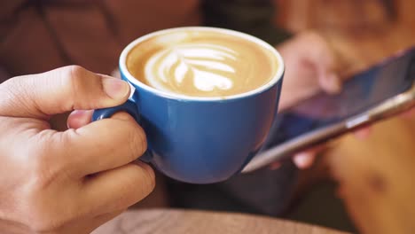 person holding a cup of latte and using a smartphone in a cafe