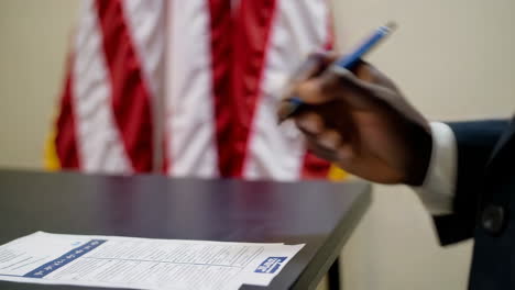 close-up of a hand writing on official documents with an american flag in the background