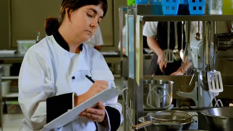 chef writing on clipboard in kitchen 4k