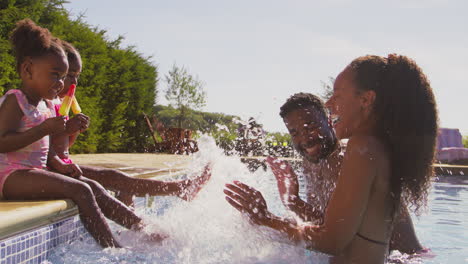 family on summer holiday with two girls eating ice lollies splashing parents in swimming pool