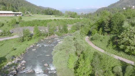 aerial flight over river with rocks flowing between forest and mountains of val di fiemme