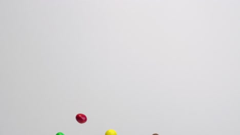 bright colored chocolate covered peanut m and m candies raining down in slow motion on white backdrop