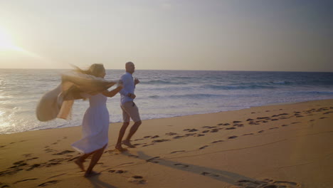 una feliz pareja descalza corriendo por la arena en la orilla del mar